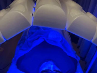 A person wearing protective eyewear beneath a blue-lit device.