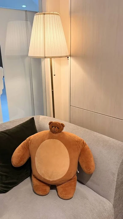 Sofa with a bear cushion beside a floor lamp, photographed by Phatchet Vittayanulak.