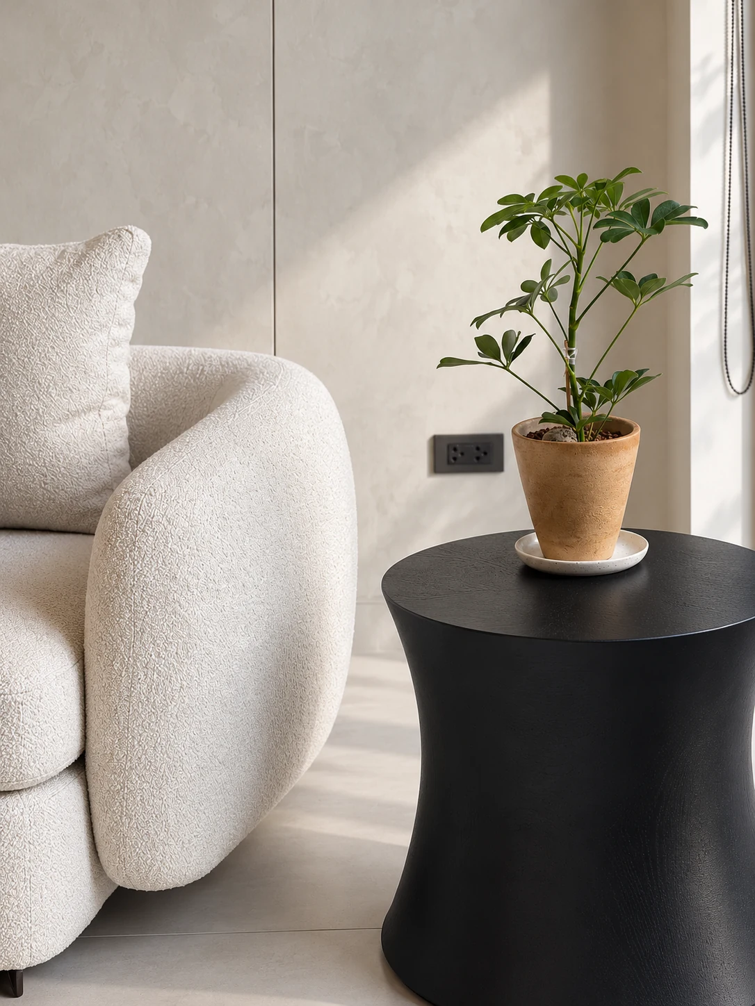 Textured ivory chair beside a dark side table and potted plant in natural light