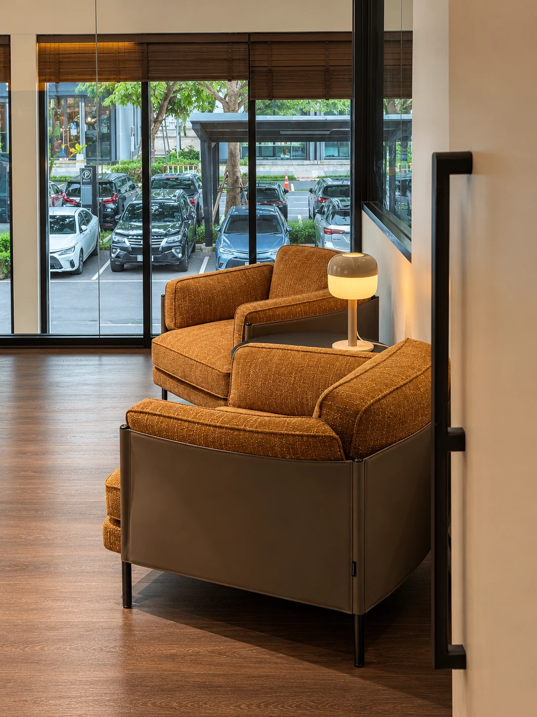 Warm-toned lounge chairs beside a softly lit table lamp and large windows